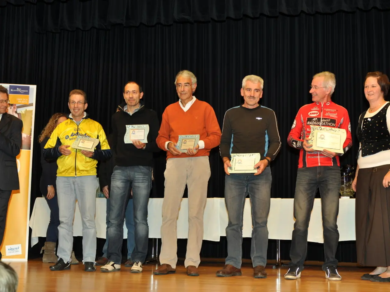 In this image we can see a group of people are standing on the stage and holding certificates in...