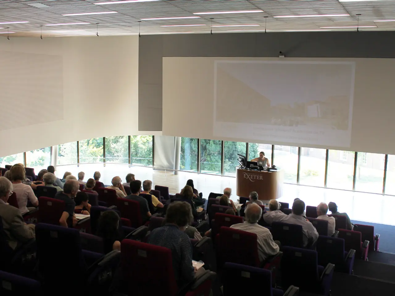 It is a seminar hall in a University , lot of people are sitting in the chairs and paying attention...