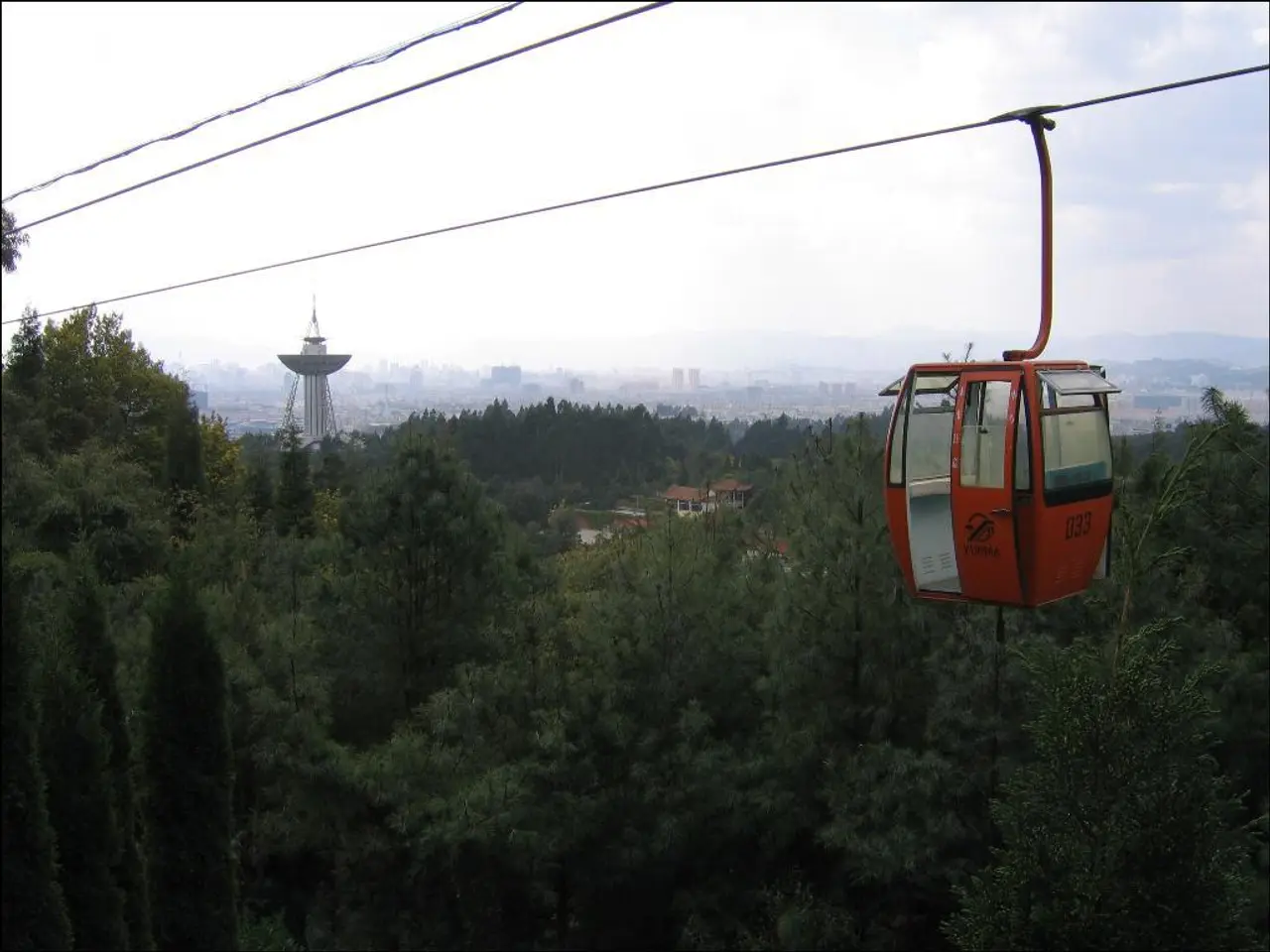 In the foreground of this image, there is a cable car moving. In the background, we see trees,...