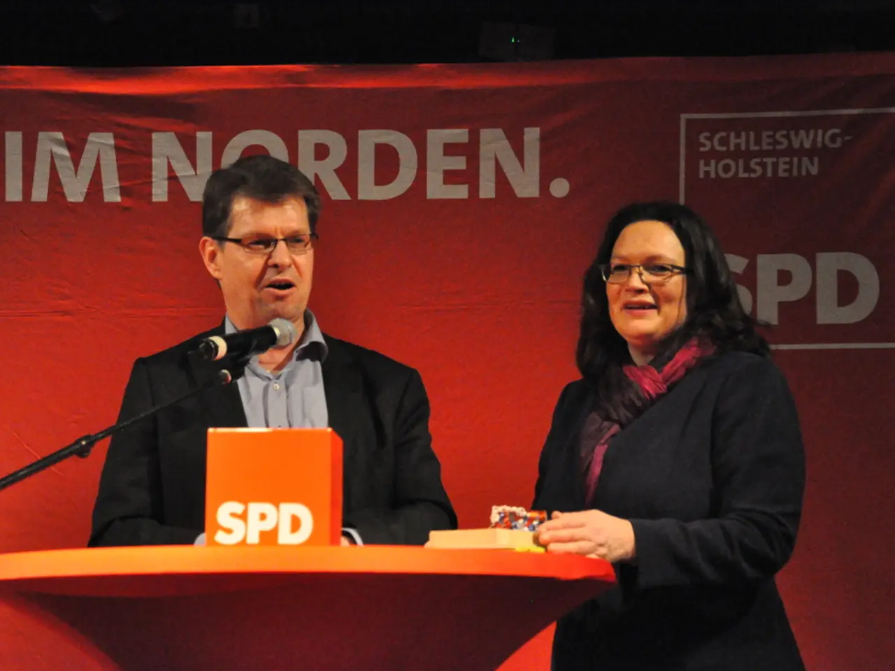 In this image we can see there are two people smiling and standing on the stage, in front of them...