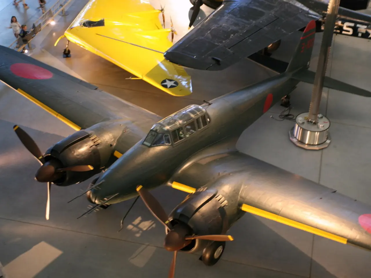 In this picture there are aircrafts. At the top left there are people and railing.