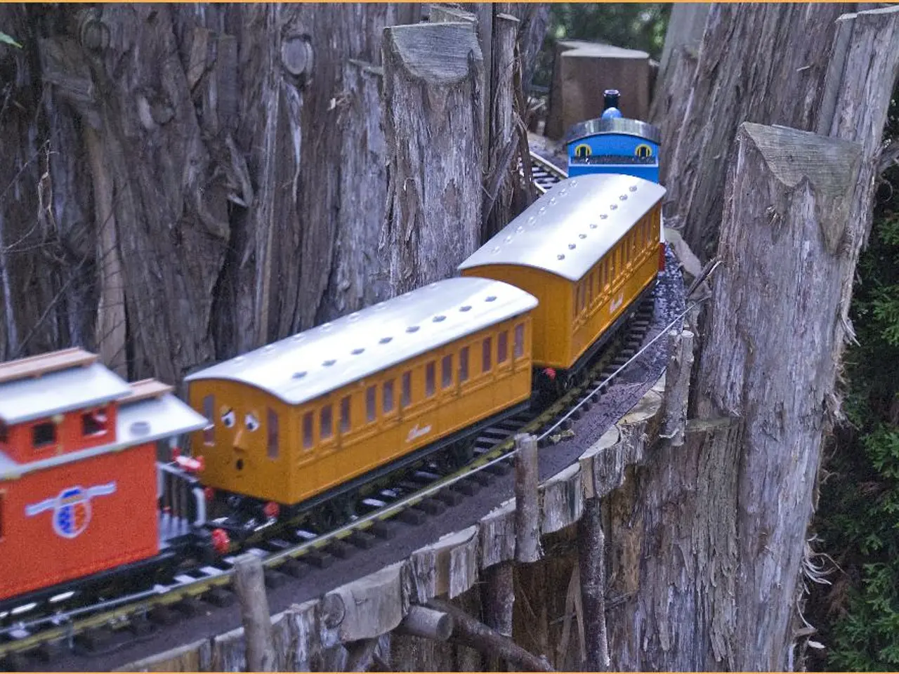 In this image we can see kids train which is moving on track in between the tree trunk and on right...