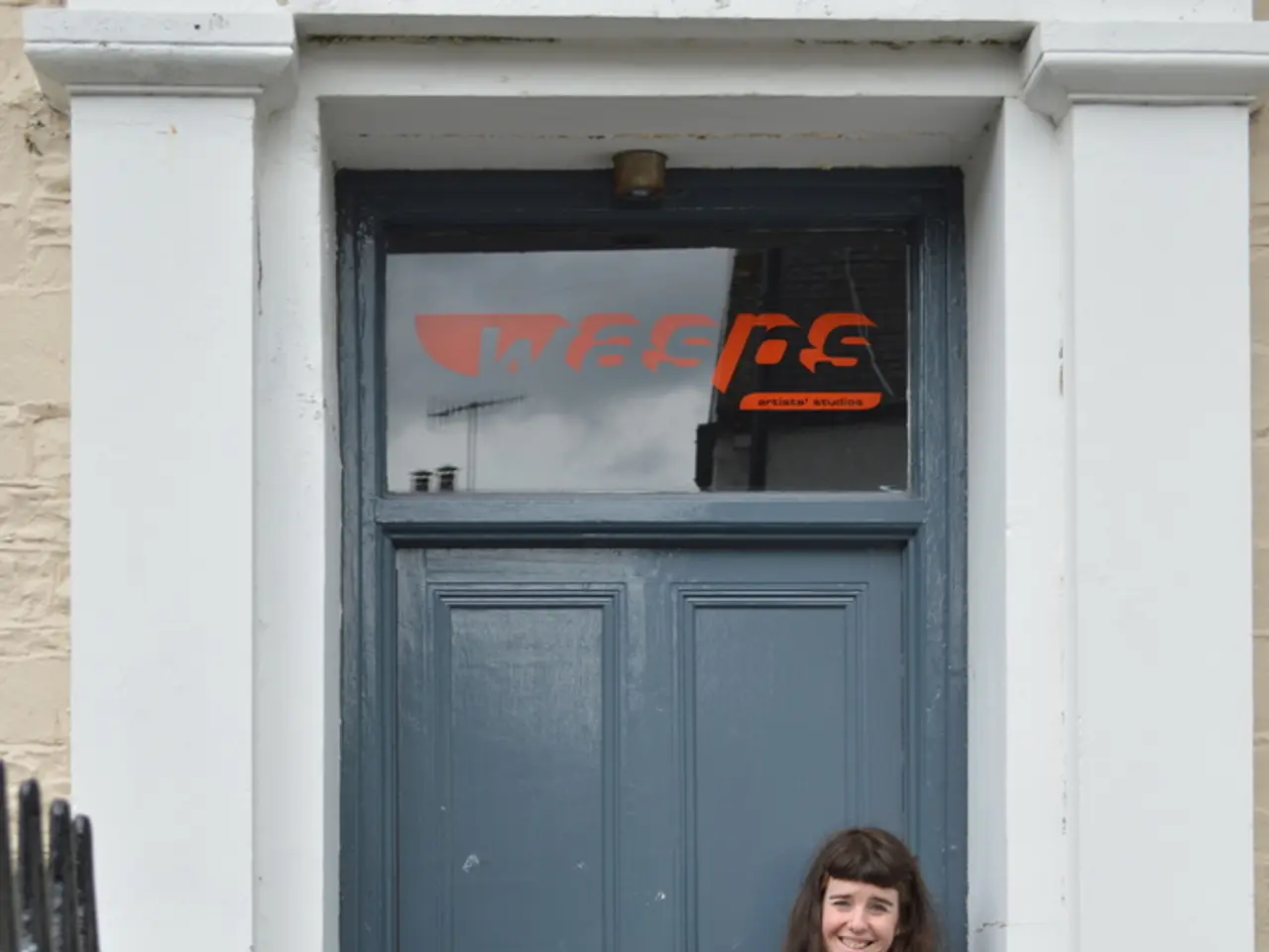 In this image there is a woman standing. She is smiling. Behind her there is a door to the wall....