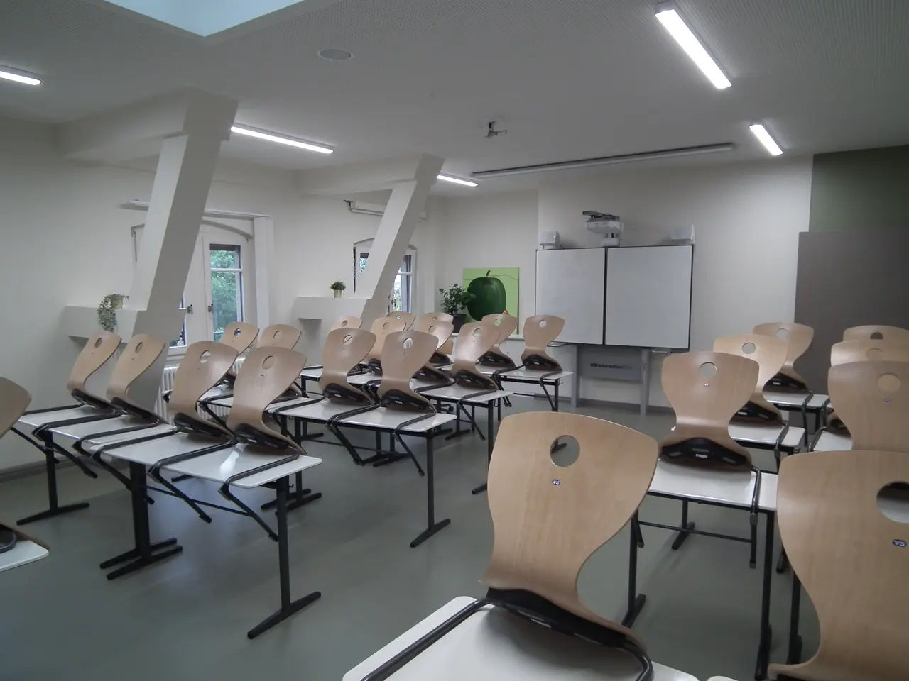 The image shows a classroom with rows of chairs arranged in neat rows, a whiteboard in the...