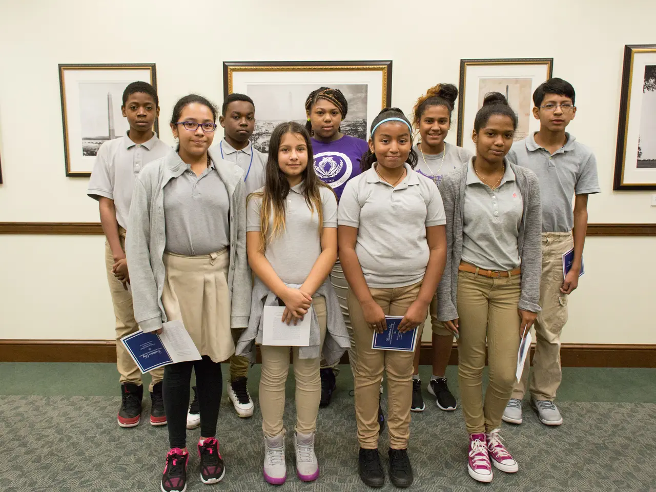 The image shows a group of young people standing next to each other in front of a wall adorned with...