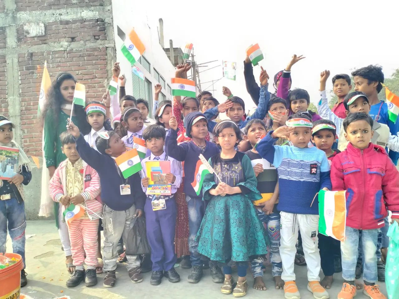 The image shows a group of children standing in front of a building, each holding an Indian flag....