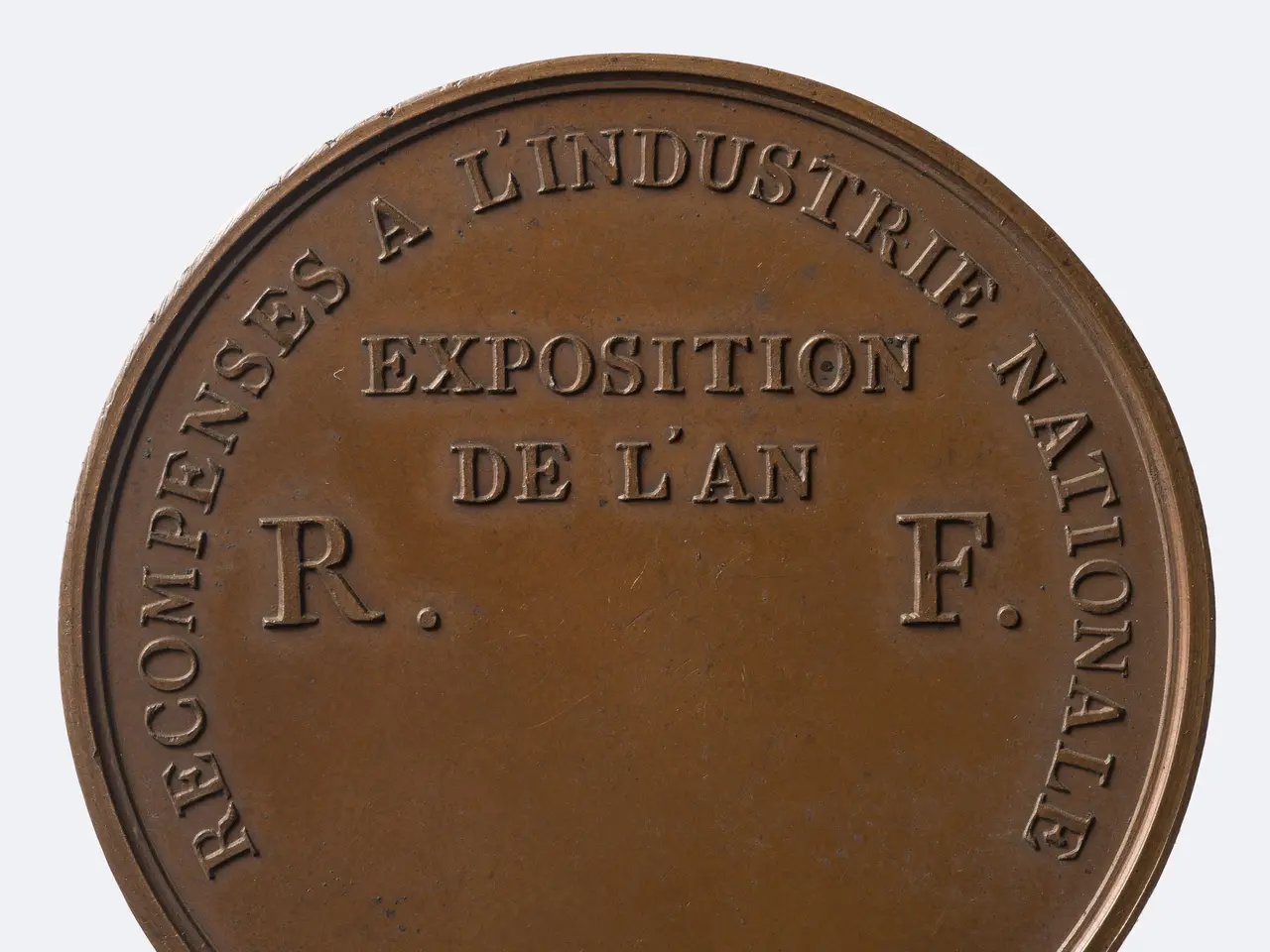 The image shows a bronze medal with the words "Recompense a l'Industrie Nationale" inscribed on it...