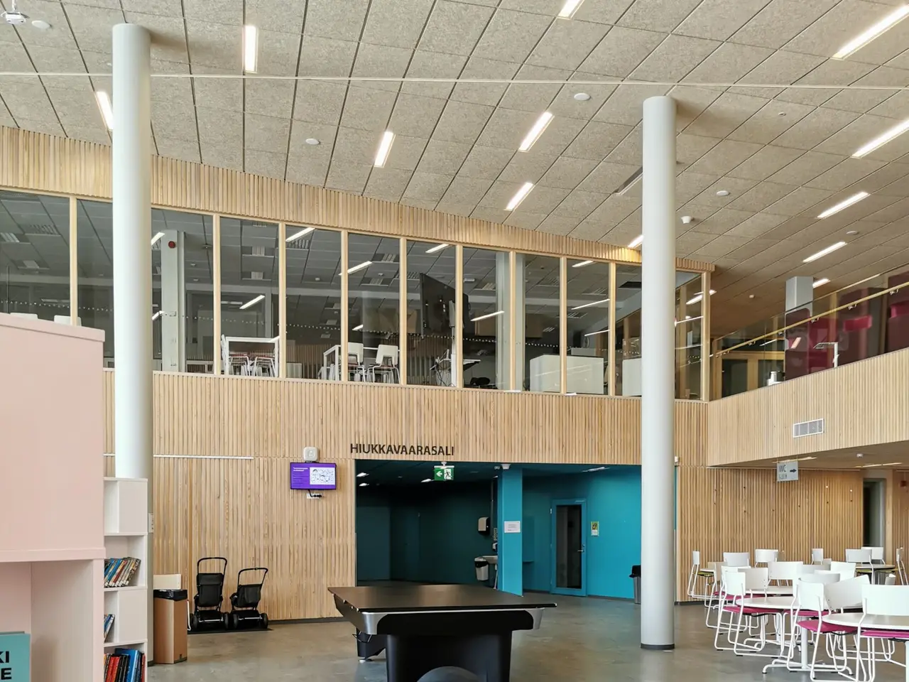 The image shows a large room filled with lots of tables and chairs, sofas, stools, bookshelves,...