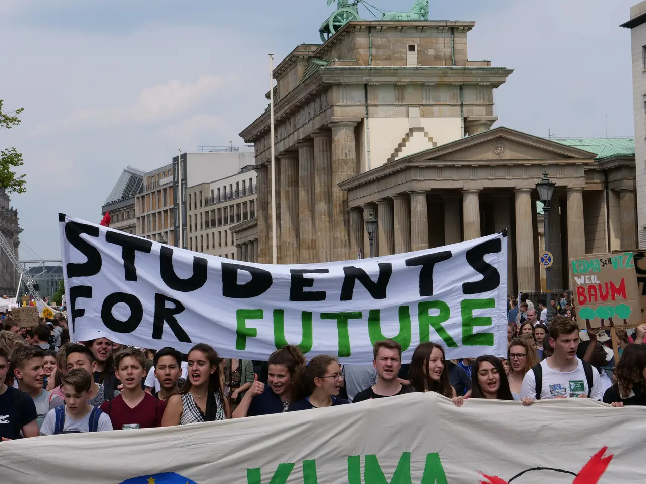 The image shows a group of students marching in Berlin, holding a banner that reads "Students for...