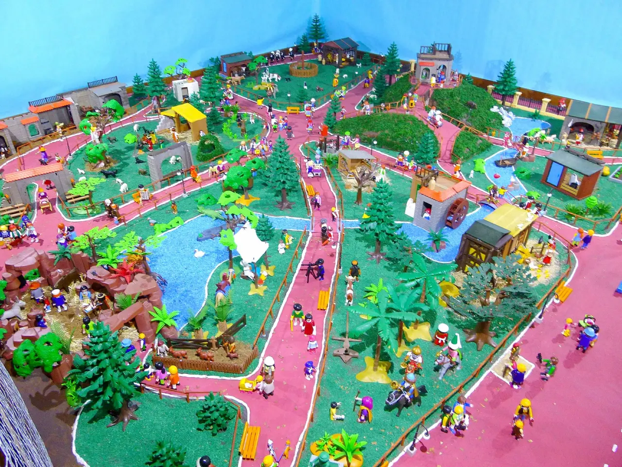 The image shows a model of a zoo with a lot of people on it, surrounded by trees, houses, plants,...