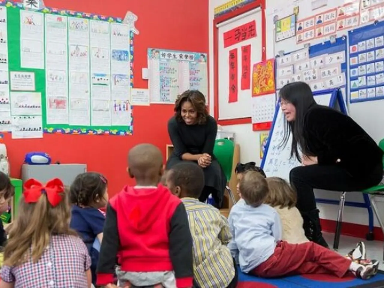 The image shows a group of children sitting on the floor in front of a teacher, who is sitting on a...