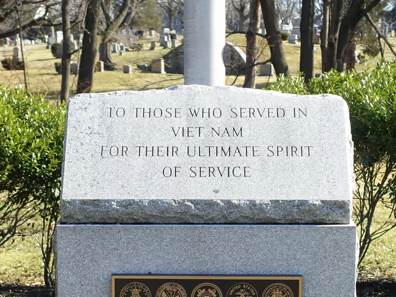 The image shows a gravestone in a cemetery with a plaque on it that reads "To those who served in...