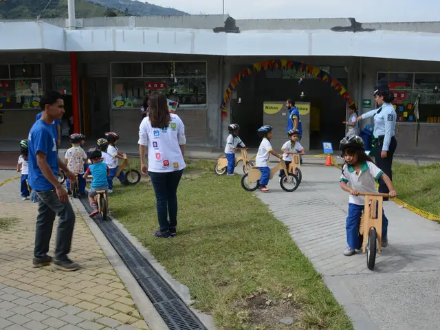 There are kids playing with cycles wearing helmets. There are some people standing over there....