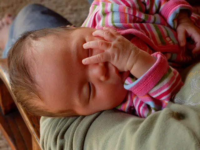 In this picture we can see a person sitting and holding a child, this child is sleeping, at the...