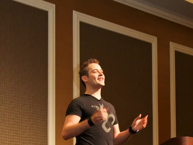 In this picture there is a man walking and smiling and we can see podium. In the background of the...