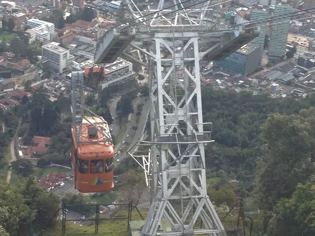 There is a tower and a cable car in the foreground area of the image, there are trees, buildings...