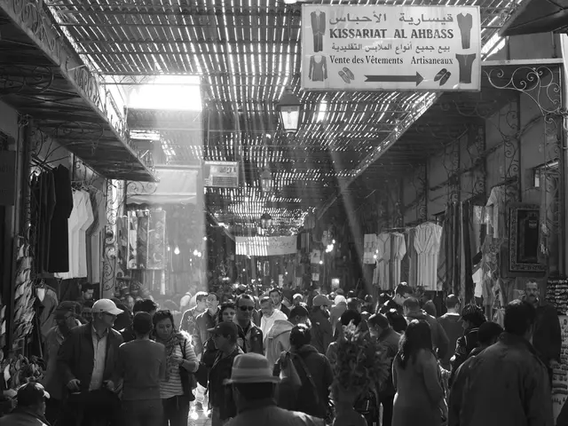 This is a black and white image in this image there are group of people on a road, on either side...