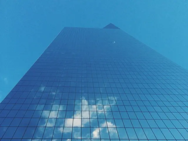 In this image there is a big glass building on which there is a reflection of clouds.
