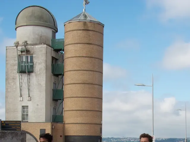 As we can see in the image there are buildings, street lamp, few people, fence, sky and clouds.