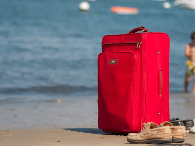 The picture is clicked on a sea where there is a red bag placed on the floor and pair of shoes. In...