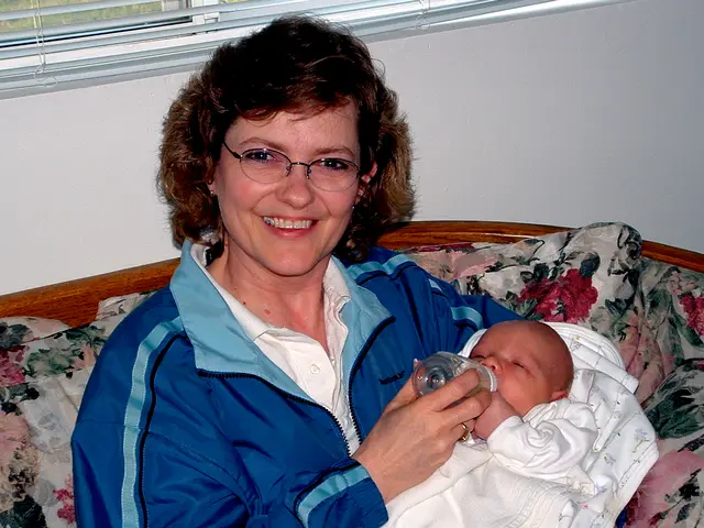 This image consists of a woman wearing a blue jacket and holding a kid. And she is feeding the...