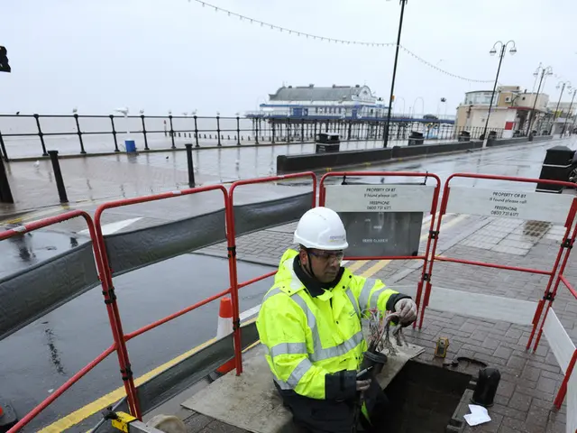 In the image there is a man with safety shirt and white helmet sitting on side of road inside a...
