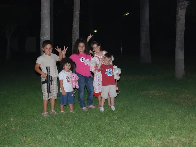 In this image I can see children are holding toys. Land is covered with grass. In the background of...