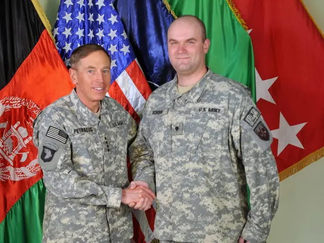 In this image there are two persons standing with a smile and they are shaken hands, behind them...