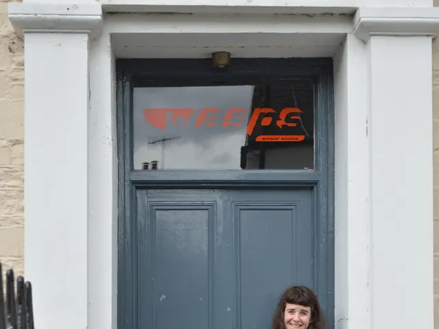 In this image there is a woman standing. She is smiling. Behind her there is a door to the wall....