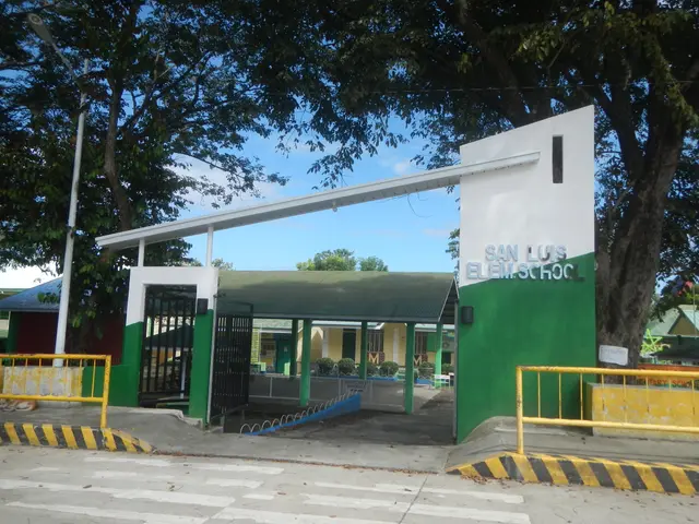 The image shows the entrance to San Luis Elementary School, with a road at the bottom, a wall with...
