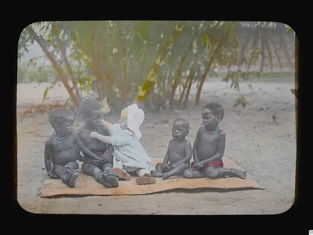 The image shows a group of children sitting on top of a blanket on the ground, surrounded by trees...