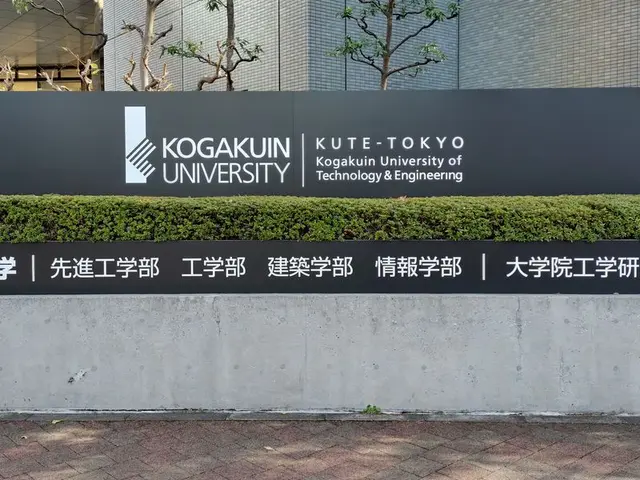 The image shows the entrance to Kogakuin University in Tokyo, Japan, with a black board with text...