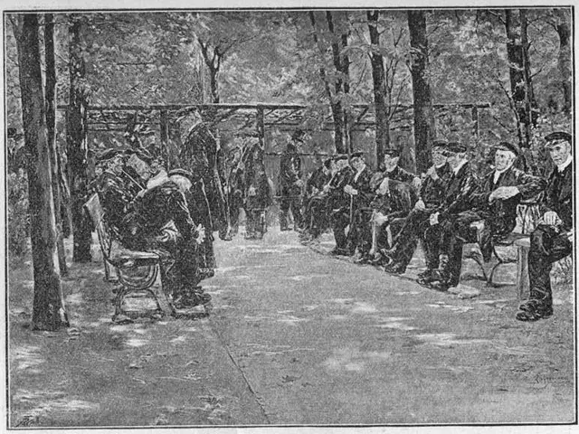 The image shows a group of people sitting on benches in a park, surrounded by trees and a shed in...