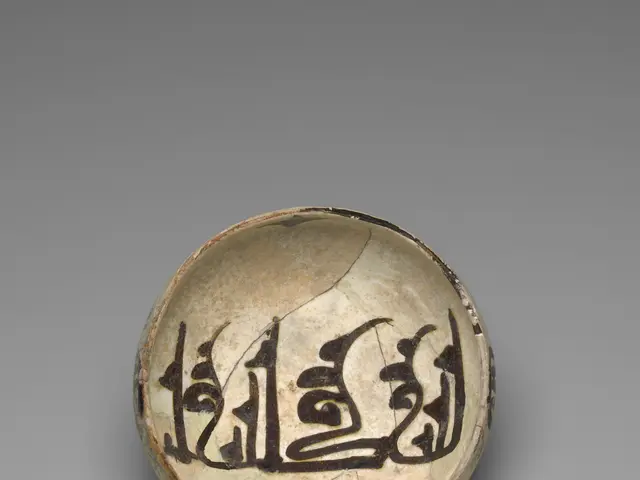 The image shows a small bowl with Arabic calligraphy on it, set against a grey background. The bowl...