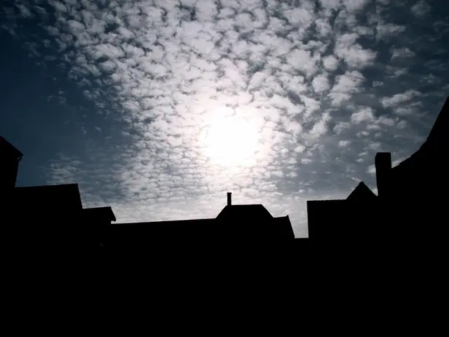 The image shows a dark sky with the sun shining through the clouds, illuminating the rooftops of...