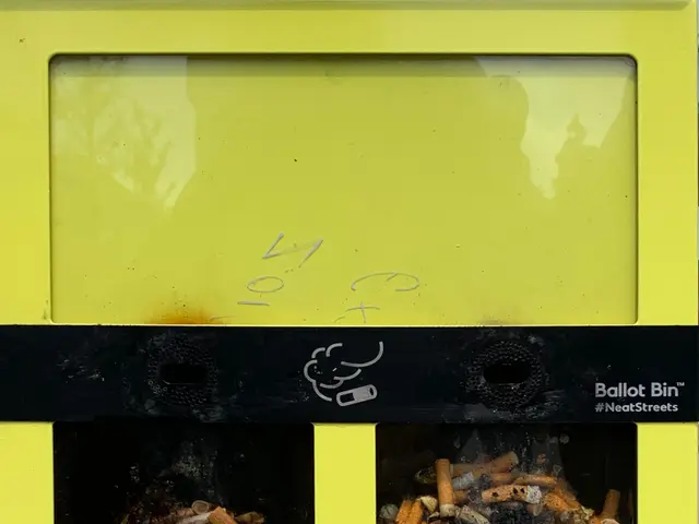 The image shows a yellow recycling bin filled with cigarette butts sitting on top of a sidewalk....