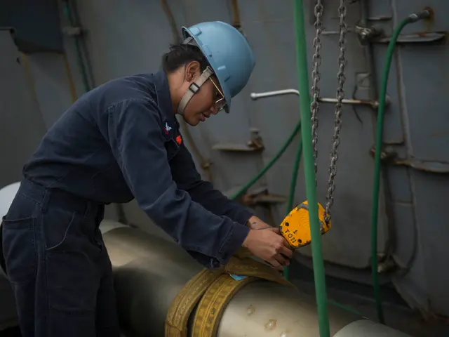 The image shows a woman in a hard hat and overalls working on a pipe, holding an object in her...
