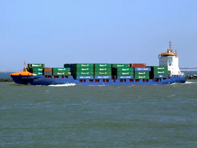 The image shows a large blue and white container ship sailing in the ocean, with many containers...