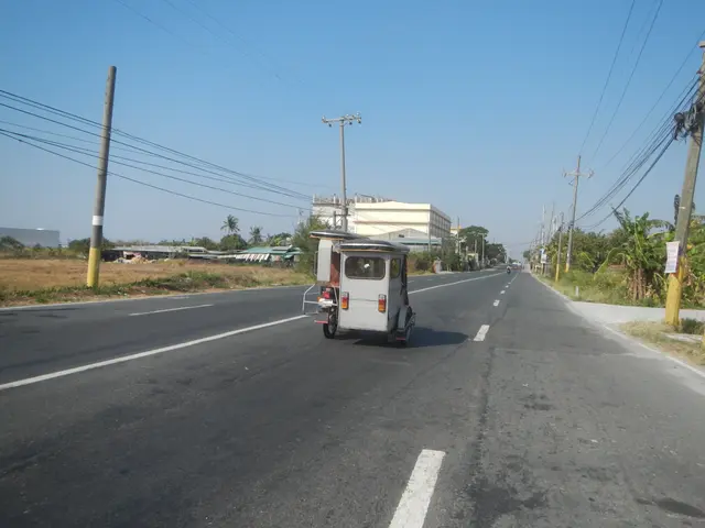 The image shows an auto rickshaw driving down a street lined with electric poles and wires, with...