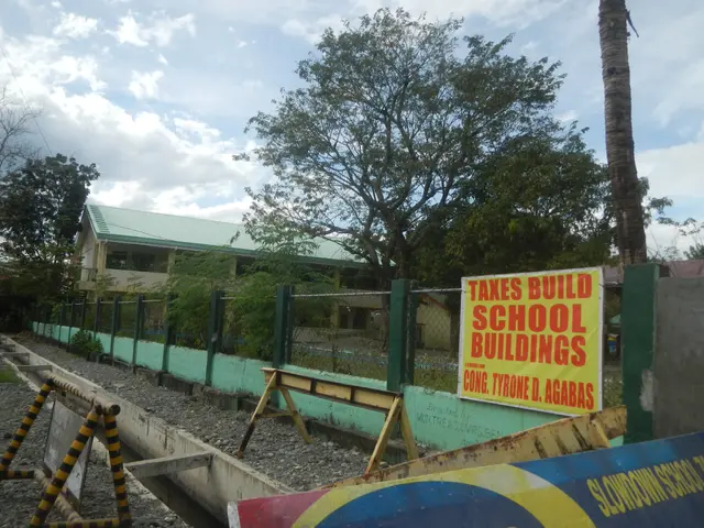 The image shows a school building with a sign that reads "Taxes Build School Buildings" surrounded...