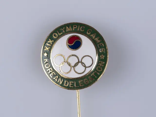 The image shows a lapel pin with the Olympic Games logo on it. The pin is circular in shape and has...