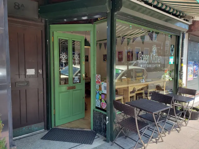 The image shows a restaurant with tables and chairs outside of it, surrounded by plants and a...