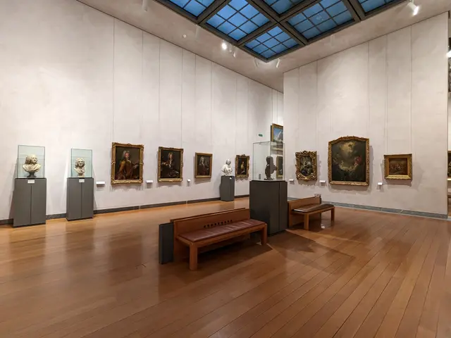 The image shows a large room filled with lots of paintings on the walls, benches on the floor,...