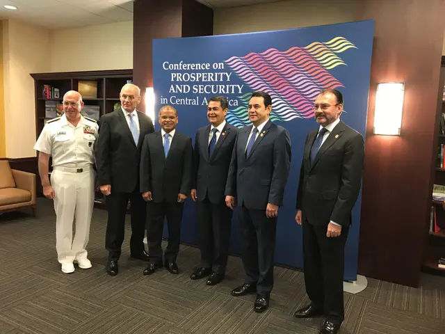 The image shows a group of men standing next to each other in front of a banner with text on it,...