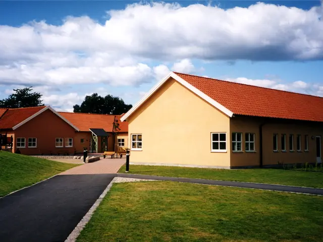 The image shows a school building with a red roof and a green lawn surrounded by houses with roofs...