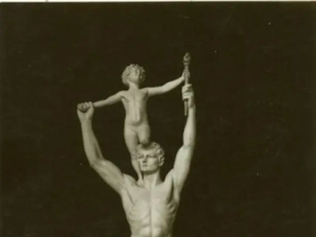 The image shows a black and white photo of a statue of a man holding a child on his shoulders, with...