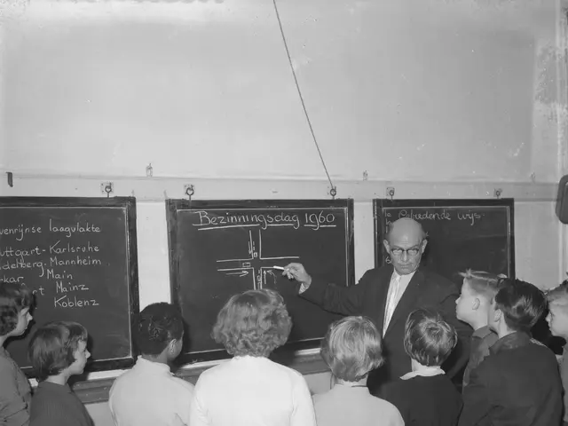 The image shows a black and white photo of a teacher teaching a class of children in a classroom....