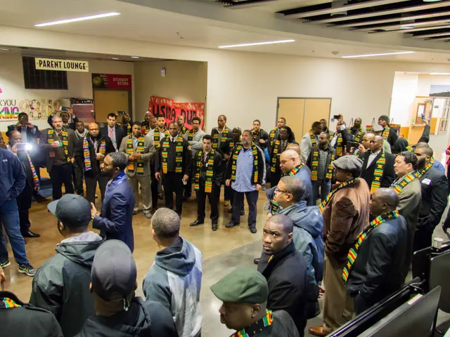 The image shows a group of people standing in front of computers in a room with a wall in the...
