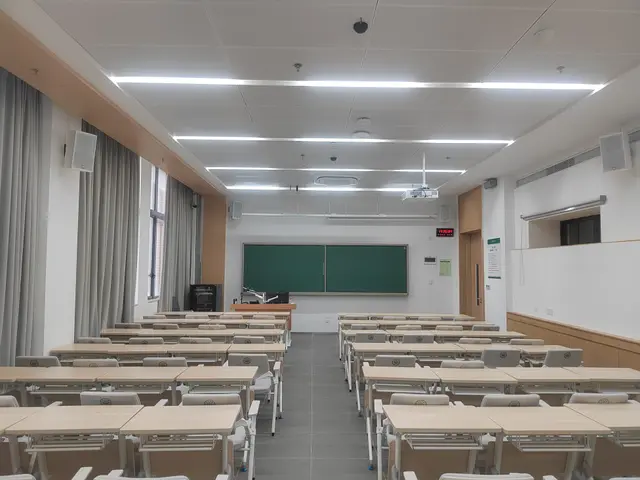 The image shows a classroom with rows of desks and chairs arranged in neat rows, a green board on...