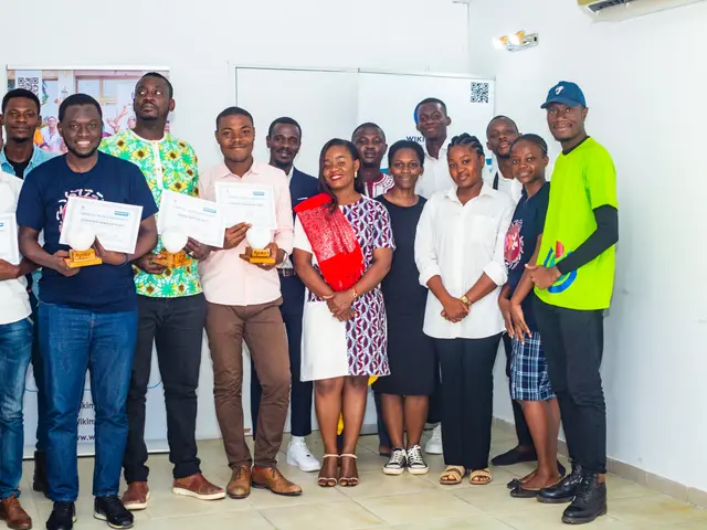 The image shows a group of people standing next to each other in a room, smiling and holding...